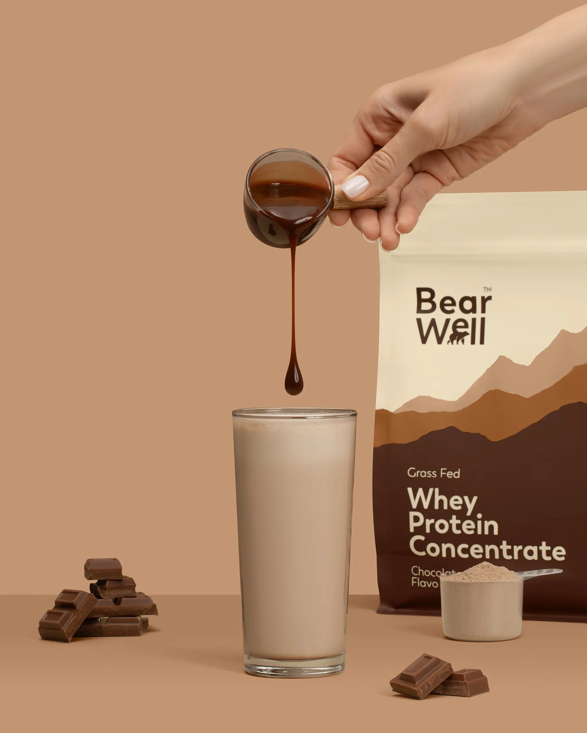 Whey Protein Concentrate Chocolate Mousse flavour with a glass of smoothie, a hand pouring a chocolate syrup and pieces of chocolate surrounding the glass