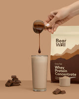 Whey Protein Concentrate Chocolate Mousse flavour with a glass of smoothie, a hand pouring a chocolate syrup and pieces of chocolate surrounding the glass