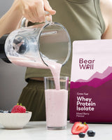 BearWell Whey Protein Isolate, Mixed Berry flavour being poured from a smoothie maker into a glass next to a bowl of fruit